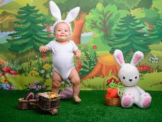 a baby standing next to two stuffed animals in front of a wall with trees and grass