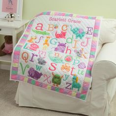 a child's personalized quilted blanket sitting on a chair next to a teddy bear