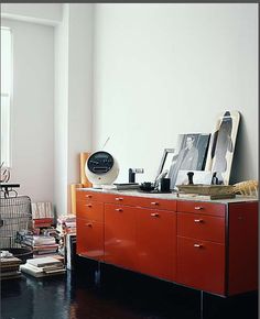 an orange cabinet in the corner of a room with books and pictures on top of it