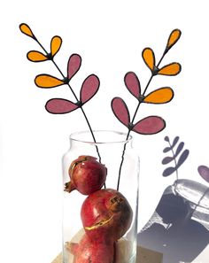 two pomegranates in a glass vase on a wooden block with leaves