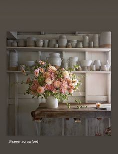 a vase filled with pink flowers sitting on top of a table next to a shelf