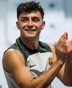 a young man is smiling and clapping his hands while wearing a jersey with the crest of barcelona on it