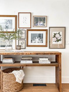 a wooden table topped with lots of pictures next to a wall filled with framed photos