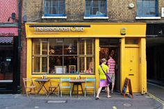 two people are standing in front of the breakfast club on a street corner with tables and chairs