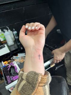 a person with a small cross tattoo on their arm and wrist, sitting in a chair