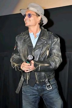 a man in a leather jacket and hat holding a microphone