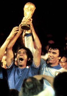 two men holding up a trophy in front of their faces while others watch from the stands