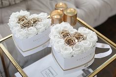 two white boxes with roses on them sitting on a glass table in front of a couch