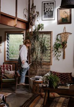 a woman standing in a living room next to a plant