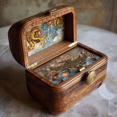 an ornate wooden box with paintings on the lid sits on a marble tablecloth covered surface