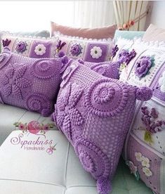 three pillows are sitting on a couch with purple crocheted designs and flowers in them