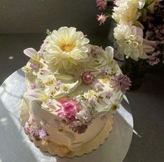 a white cake with pink and yellow flowers on it sitting on top of a table