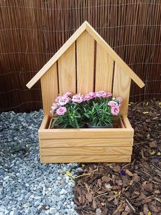 a wooden birdhouse filled with pink flowers on top of gravel next to a fence