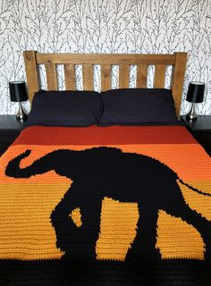 an elephant crocheted blanket on top of a bed in a room with wallpaper