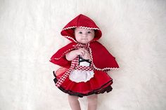 a baby girl dressed in a red and white dress with a hood on her head