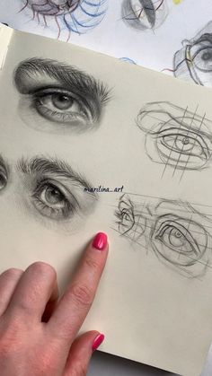 a woman's hand is pointing at an open book with sketches of eyes and eyebrows