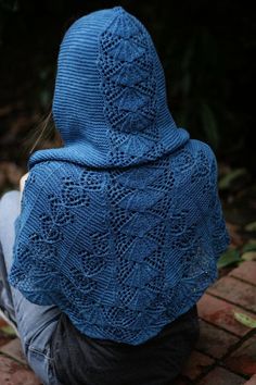 a person sitting on the ground wearing a blue knitted shawl over their head