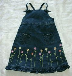 a denim dress with flowers embroidered on the front and back, sitting on a white blanket