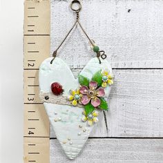 a heart shaped decoration hanging on a wall next to a measuring ruler with flowers and leaves