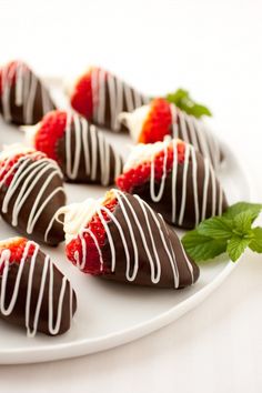 chocolate covered strawberries are arranged on a white platter with mint sprigs