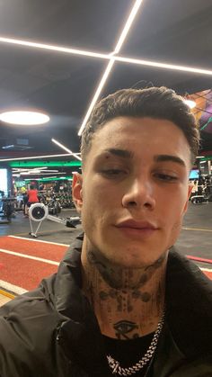 a man with tattoos on his face and chest standing in a gym area looking at the camera