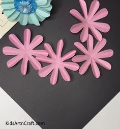 some pink and blue flowers are sitting on a black surface next to a paper flower