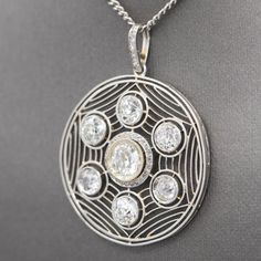 This enticing Art Deco pendant shows like a spider's web with a center round Old Mine cut diamond surrounded by a small halo and framed by six smaller Old Mine cut diamonds. In between the stones are mill grained rows lie spider's web connecting the stones. The center stone rests in a mirror-edge bezel, surrounded a halo of small rose cut diamonds and measures approximately 6.4 mm (carat weight is approx .93 carats); surrounding OMC diamonds measure 4.6 - 5 mm (carat weights are approx .58 carat Fine Jewelry Diamond Necklace With Intricate Design, Intricate Diamond Round Pendant Jewelry, Diamond Round Pendant With Intricate Design, Diamond Jewelry With Intricate Design In Round Pendant, Art Deco Diamond Pendant Necklace With Accents, Art Deco White Gold Necklace With Rose Cut Diamonds, Round Diamond Necklace With Intricate Design, Antique Round Necklace With Diamond Accents, Art Deco Diamond Necklace With Diamond Accents