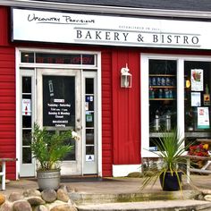 a red building with white trim and windows has plants in pots outside the door, and there is a sign that says bakery & bistro