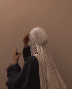 a woman with a white veil on her head standing in front of a wall holding a cell phone