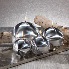 three silver candles sitting on top of a metal tray next to a piece of wood