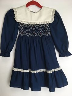 Vintage 1970s Polly Flinders hand smocked dress Size 4 ~Navy blue with white collar and lace details ~Hand smocked bodice w/ rosebud pattern ~Sailor collar ~Long sleeves ~65% polyester/35% cotton ~Button closure w/ tie on back ~Made in St Vincent ~No rips, tears, stains, or odors Hand Smocked Dress, Vintage Sailor, St Vincent, Hand Smock, Sailor Collar, Smocked Dress, Dress Vintage, White Collar, Rose Buds