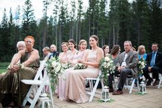 a group of people sitting next to each other on white chairs in front of trees