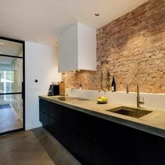 a kitchen with a stone wall and black cabinets, an island sink and a wine bottle on the counter