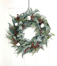 a wreath hanging on the front door decorated with greenery and pineconis for christmas