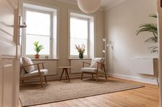 a living room with two chairs and a table in front of the window, next to a potted plant