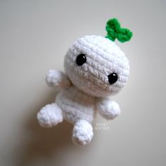 a small crocheted white stuffed animal with a green leaf on its head and eyes