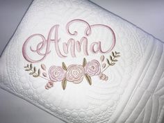 an embroidered name on the back of a white pillow with pink flowers and leaves around it