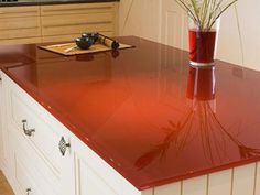 a red counter top in a kitchen next to a vase with some flowers on it