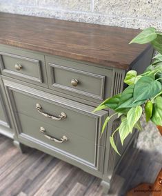 a green dresser with wooden top next to a potted plant