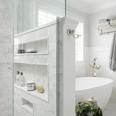 a white bathtub sitting next to a sink in a bathroom with marble walls and floors