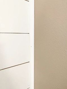 a cat sitting on the corner of a room next to a white door and wall