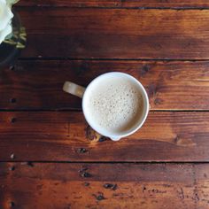 a cup of coffee sitting on top of a wooden table next to a vase with flowers