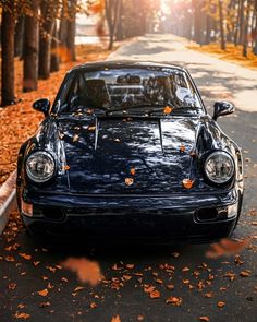 a blue sports car parked on the side of a road with leaves all over it