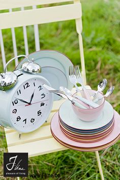 a stack of plates sitting next to a clock on top of a wooden chair in the grass