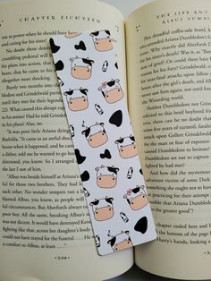 a bookmark with cows on it sitting in front of an open book that is laying down