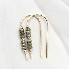 Up your earring game with Cheval—gold threaders with a pop of sage green Miyuki seed beads. Whether you're looking for subtle shine, a bit of boho, or just something to perk up your lobes, this pair of sparkly beauties is the answer! 14k Gold Filled Measure approximately 1.25 Inches Quality Miyuki Seed Beads Sent in a Ribboned Gift Box Handmade in Montana Brass Jewelry With Tiny Beads In Dangle Shape, Gold Tiny Beads Drop Earrings, Gold Drop Earrings With Tiny Beads, Bohemian 14k Gold Filled Earrings With Tiny Beads, Everyday Adjustable Nickel-free Threader Earrings, 14k Gold-filled Tiny Beaded Earrings, Handmade Minimalist 14k Gold Filled Threader Earrings, Minimalist Everyday Jewelry With Dangling Beads, Everyday Minimalist Jewelry With Dangling Beads