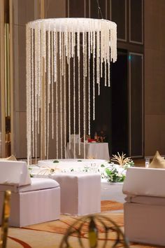 a chandelier hanging from the ceiling in a room filled with white couches and tables