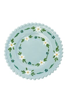 a blue plate with white flowers and green leaves on the rim, against a white background