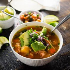 two bowls filled with soup sitting on top of a wooden table next to sliced avocado