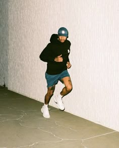 a man in black shirt and blue shorts running on cement floor next to white wall